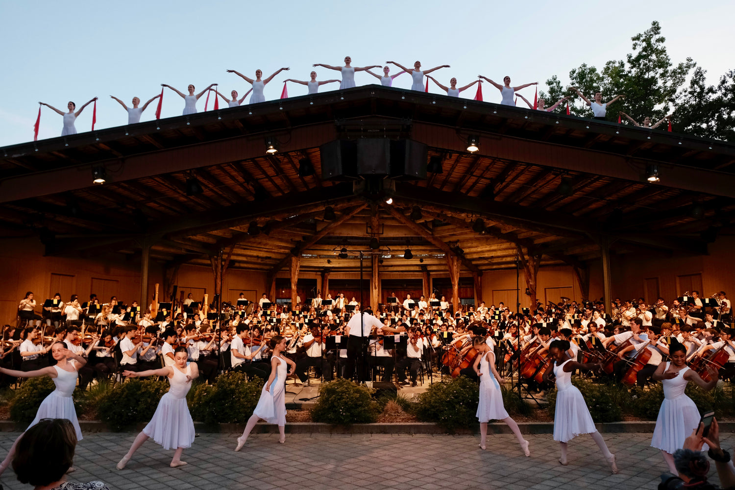 Orchestra performing on a stage with dancers in front and on top of roof