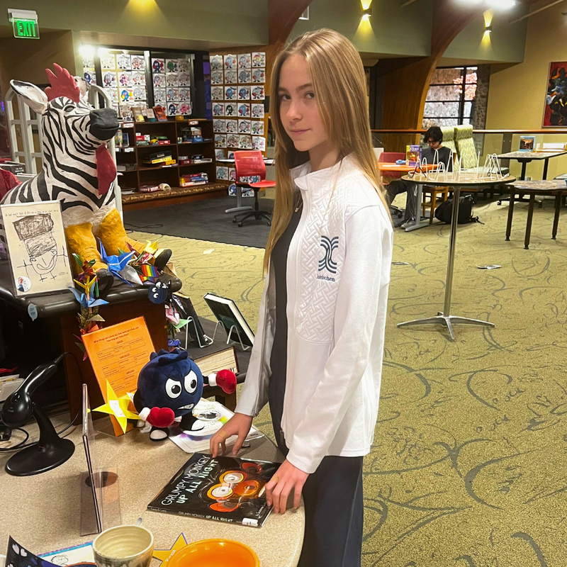 Person holding a book in a library setting with decorative items and tables.