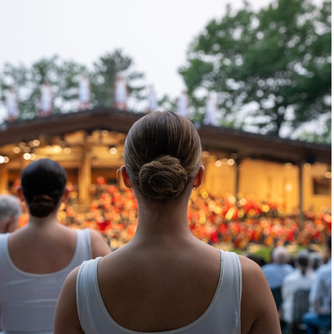 Two women facing a stage with a blurred audience in the background