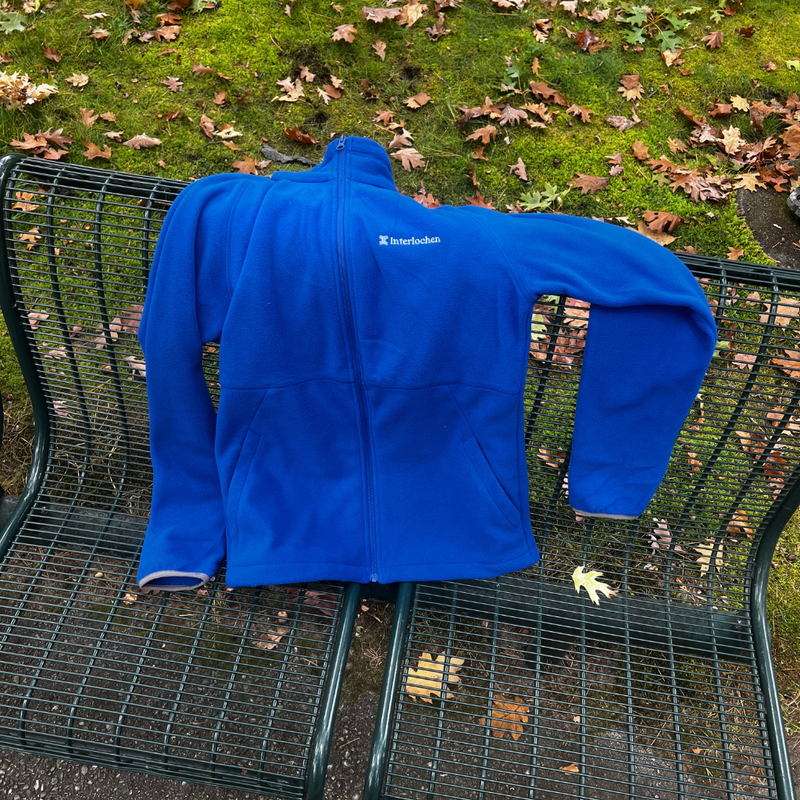 Blue jacket with a brand logo on a metal bench outdoors.