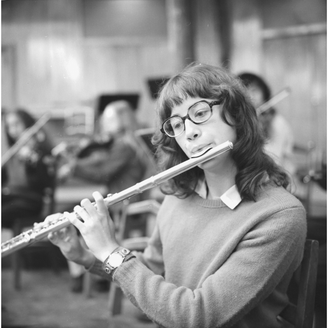 Person playing the flute in a recording studio with musical equipment in the background