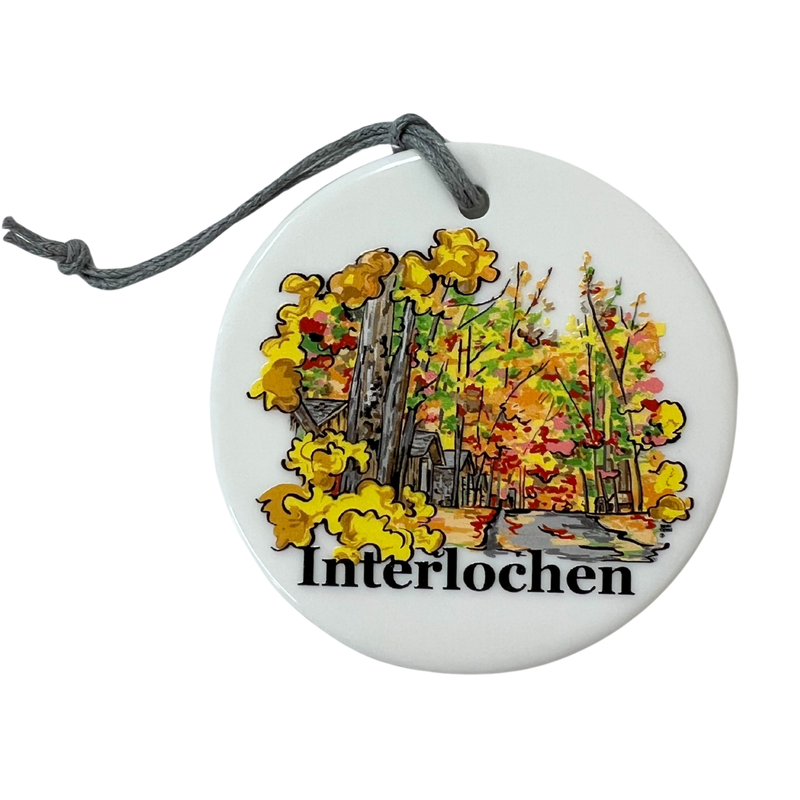 Round ceramic ornament with 'Interlochen' design featuring flowers and a pond on a white background.