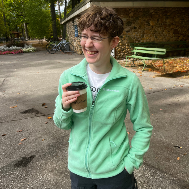 Person wearing a light green jacket holding a coffee cup outdoors.
