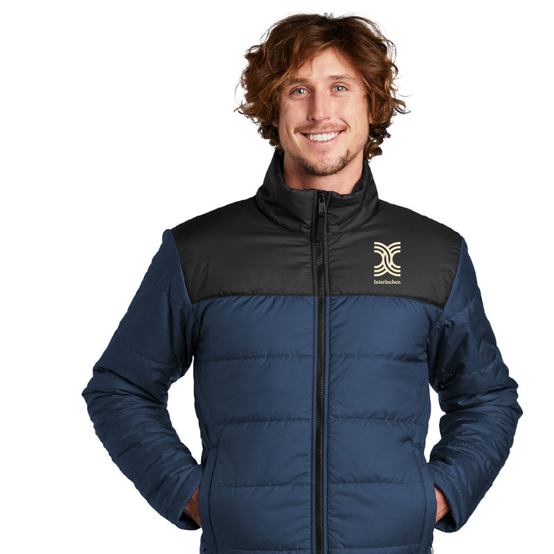 A man smiling, wearing a North Face Interlochen Insulated Jacket in navy color with a logo on the chest.